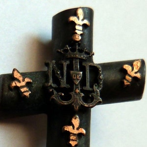 May include: A bronze cross with a gold-colored 'N.D.' monogram and fleur-de-lis accents.
