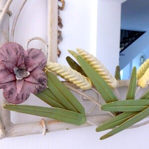 May include: White metal mirror with a floral design. The mirror has a pink flower, green leaves, and yellow wheat stalks.