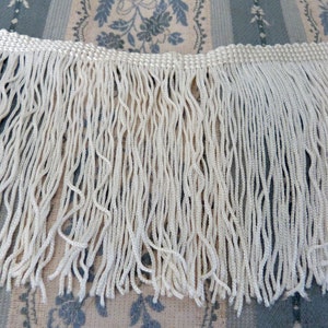 May include: White fringe trim with a woven edge. The fringe is approximately 1 inch long.