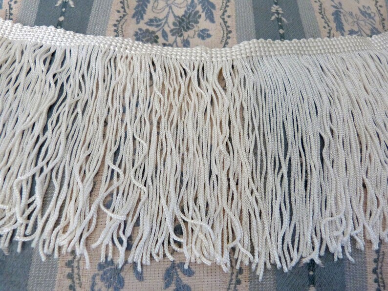May include: White fringe trim with a woven edge. The fringe is approximately 1 inch long.