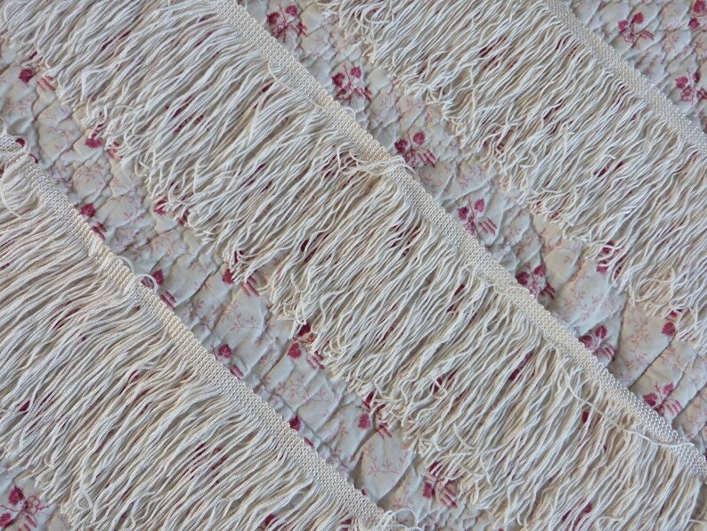 May include: Close-up of white cotton fringe trim. The fringe is thick and fluffy, with a slightly uneven texture.