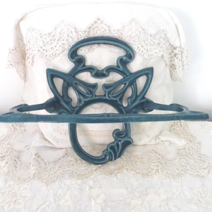 May include: A teal-coloured metal towel rack with an Art Nouveau design. The rack has a curved handle and a horizontal bar for towels. The design includes stylised floral and geometric shapes. The rack is made of metal.