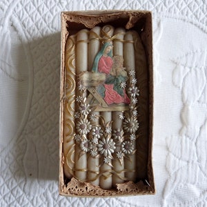 May include: A set of white candles in a box with a religious image of Mary and baby Jesus. The candles are decorated with gold and silver accents and white flowers.