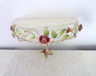 May include: Off-white metal wall shelf with a semi-circular design. The shelf is adorned with painted metal leaves, red flowers, and small orange accents. The shelf is designed for decorative purposes.