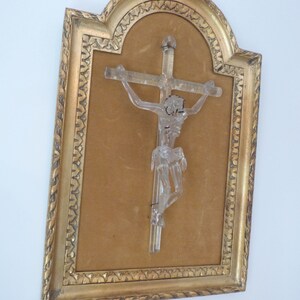 May include: A glass crucifix in a gold-colored frame with a brown velvet backing. The frame has a decorative design around the edge.
