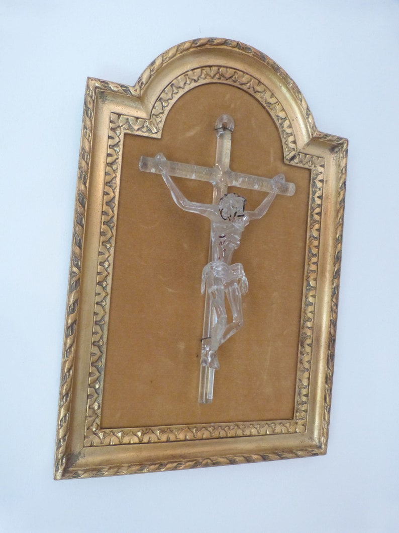May include: A glass crucifix in a gold-colored frame with a brown velvet backing. The frame has a decorative design around the edge.