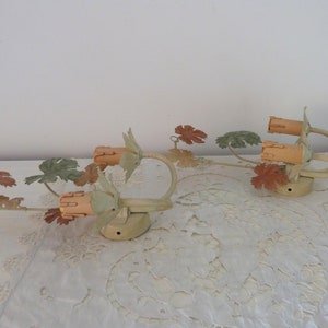 May include: Two vintage wall sconces with a leafy vine design. The sconces are painted in a light green and brown color scheme. Each sconce has two light bulbs.