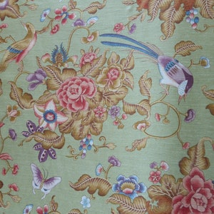 Pode incluir: Tecido verde com um padrão floral com flores rosa, roxas e azuis, folhas marrons e dois pássaros. O tecido tem o texto "Christian Lacroix - Paris" e "Belfort" impresso na lateral.