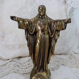 Op de afbeelding: Een gouden beeld van Jezus Christus met zijn armen uitgestrekt. Hij draagt een gewaad en heeft een hart op zijn borst.
