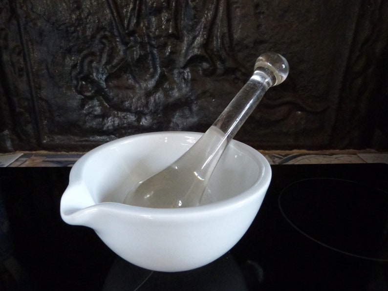 May include: A white ceramic mortar and pestle set with a clear glass pestle. The mortar has a spout for pouring.