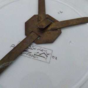 May include: Close-up of the back of a white porcelain plate with a brass plate holder. The plate has a black ink inscription that reads "D.V.X.I.V. 21".