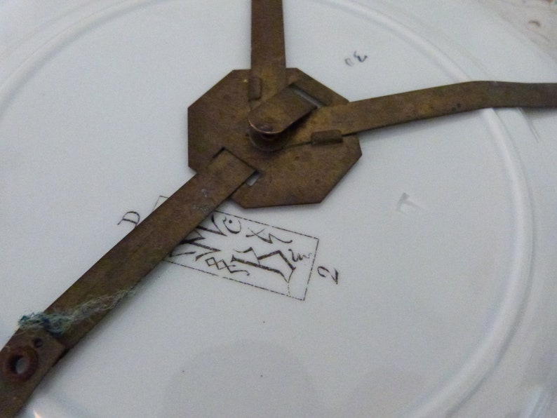 May include: Close-up of the back of a white porcelain plate with a brass plate holder. The plate has a black ink inscription that reads "D.V.X.I.V. 21".