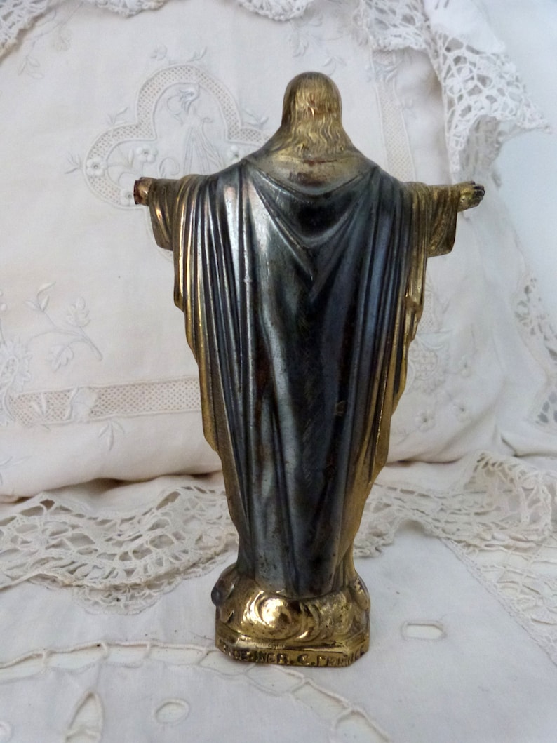 Op de afbeelding: Een klein, goud geverfd metalen beeld van Jezus Christus met uitgestrekte armen. Het beeld staat op een voet met de inscriptie "Breiner, C. France".