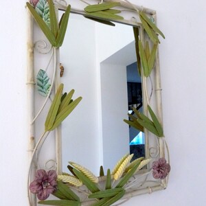 May include: A white metal mirror with a decorative frame featuring green and yellow leaves and pink flowers.