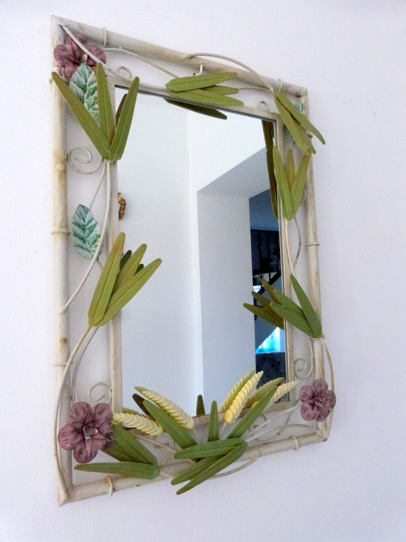 May include: A white metal mirror with a decorative frame featuring green and yellow leaves and pink flowers.
