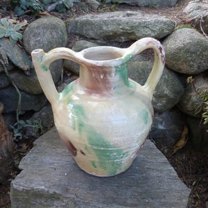 May include: A large, yellow ceramic pitcher with two handles and a spout. The pitcher has a green, brown, and white glaze.