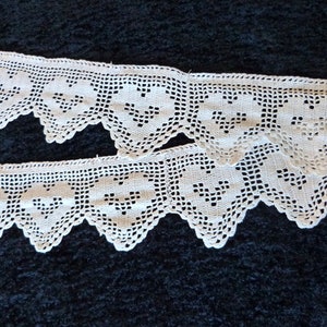 May include: Two pieces of white crocheted lace trim with a scalloped edge and a repeating heart pattern.