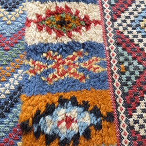 Op de afbeelding: Close-up van een kleurrijk Marokkaans tapijt met ingewikkelde geometrische patronen in tinten blauw, rood, wit en oranje.