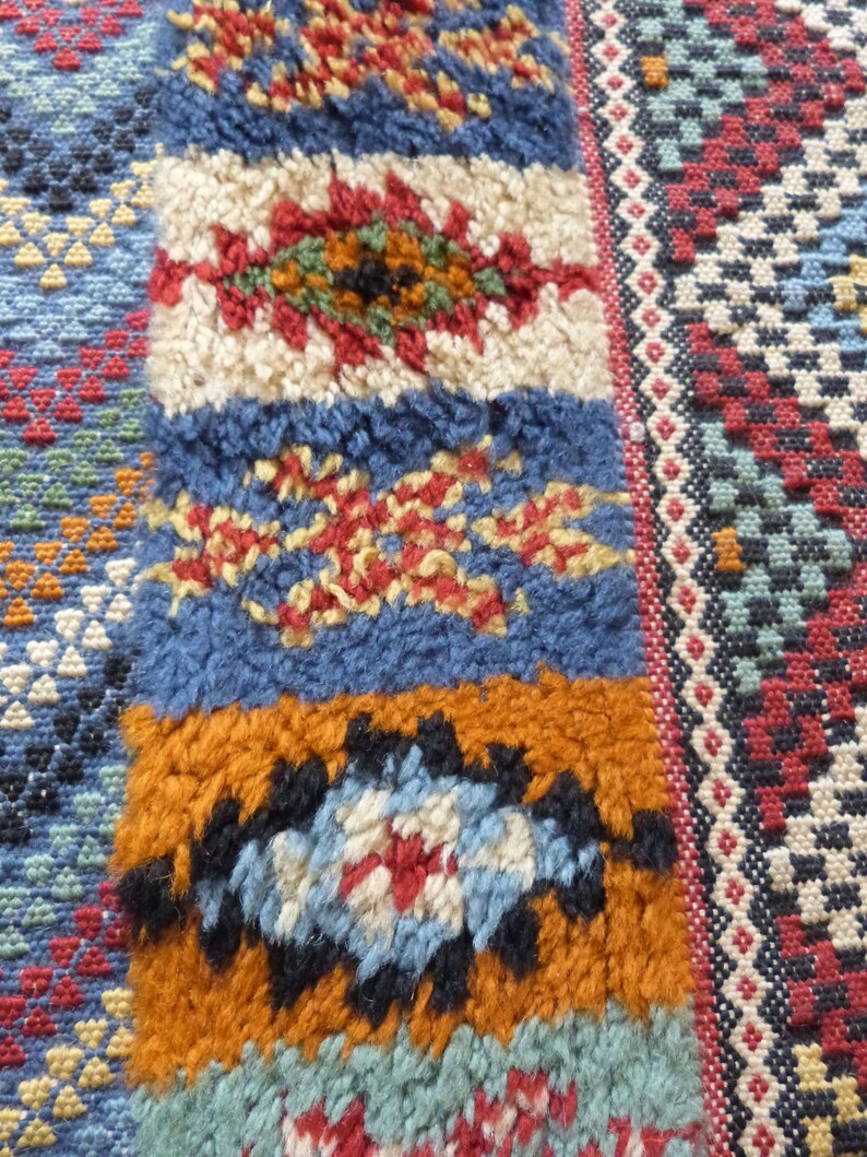 Op de afbeelding: Close-up van een kleurrijk Marokkaans tapijt met ingewikkelde geometrische patronen in tinten blauw, rood, wit en oranje.