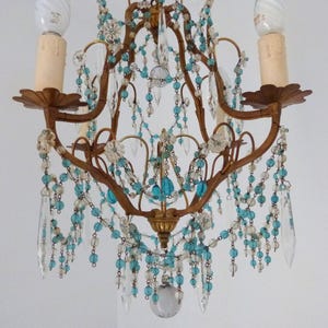May include: An antique chandelier with a bronze frame, adorned with clear and turquoise beads and crystal pendants. The fixture has two candle-style bulb holders and decorative floral accents, creating an elegant, vintage aesthetic.