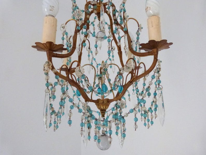 May include: An antique chandelier with a bronze frame, adorned with clear and turquoise beads and crystal pendants. The fixture has two candle-style bulb holders and decorative floral accents, creating an elegant, vintage aesthetic.