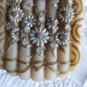 May include: A vintage white and gold decorative box with a floral design. The box has a raised floral design with silver and gold accents. The box is made of a hard, smooth material.