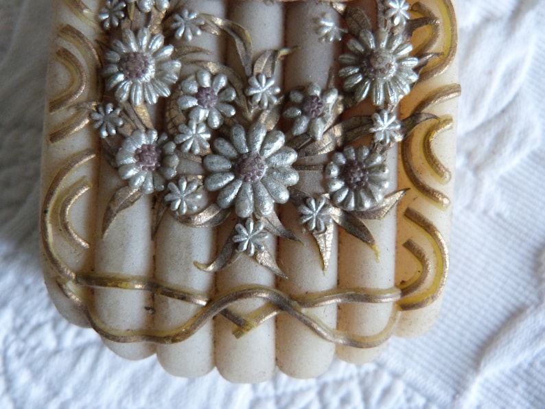 May include: A vintage white and gold decorative box with a floral design. The box has a raised floral design with silver and gold accents. The box is made of a hard, smooth material.