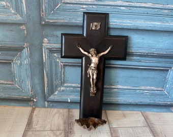 May include: A black wooden crucifix with a silver Jesus figure. The crucifix has a small shelf at the bottom and a small plaque with the inscription "INRI" at the top.