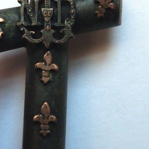 May include: A black metal cross with gold fleur-de-lis accents and the letters "N.D." in the center.