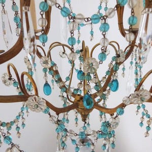 May include: Close-up of a vintage chandelier with a gold-toned metal frame. The chandelier is adorned with clear and turquoise-colored beads and crystal teardrops. The design includes floral accents and curved arms.