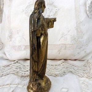 Op de afbeelding: Een gouden beeld van Jezus Christus met zijn armen uitgestrekt. Het beeld staat op een voetstuk met een decoratief ontwerp.