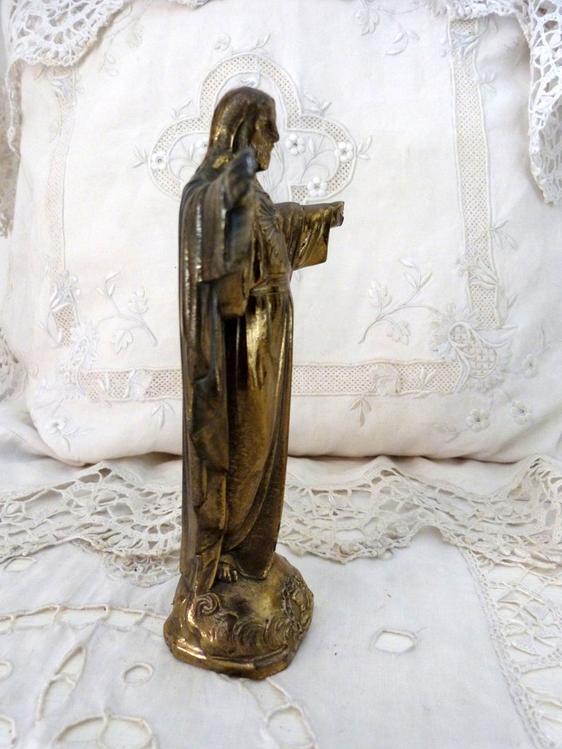 Op de afbeelding: Een gouden beeld van Jezus Christus met zijn armen uitgestrekt. Het beeld staat op een voetstuk met een decoratief ontwerp.