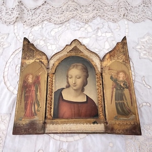 May include: An antique triptych painting featuring a central portrait of a woman in a red dress, flanked by images of angels. The artwork is set against a gold background and framed in a weathered, ornate wooden structure.