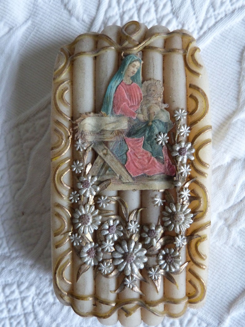 May include: A white candle with a raised design of a nativity scene with Mary, Joseph, and baby Jesus. The candle is decorated with gold and silver flowers.