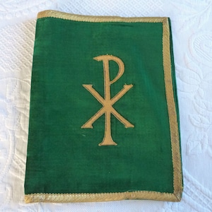 Può includere: Una copertina di libro in velluto verde con un simbolo Chi Rho ricamato in oro. La copertina ha un bordo dorato.