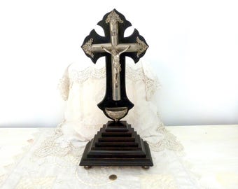 May include: A dark wooden crucifix with a silver figure of Jesus Christ. The cross has ornate silver detailing and is mounted on a stepped, dark wooden base. A small silver bowl is below the figure.