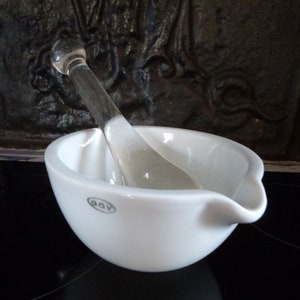 May include: White porcelain mortar and pestle set with a glass pestle. The mortar has a small spout and the brand name "GOV" is printed on the bottom.