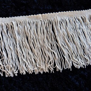 May include: White fringe trim with a woven edge. The fringe is approximately 1 inch long.