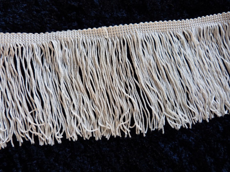 May include: White fringe trim with a woven edge. The fringe is approximately 1 inch long.