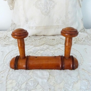 Puede incluir: Un perchero de madera vintage con dos pomos redondeados y una barra horizontal. El perchero es de madera marrón claro con detalles en marrón oscuro y probablemente sea un artículo antiguo o vintage.
