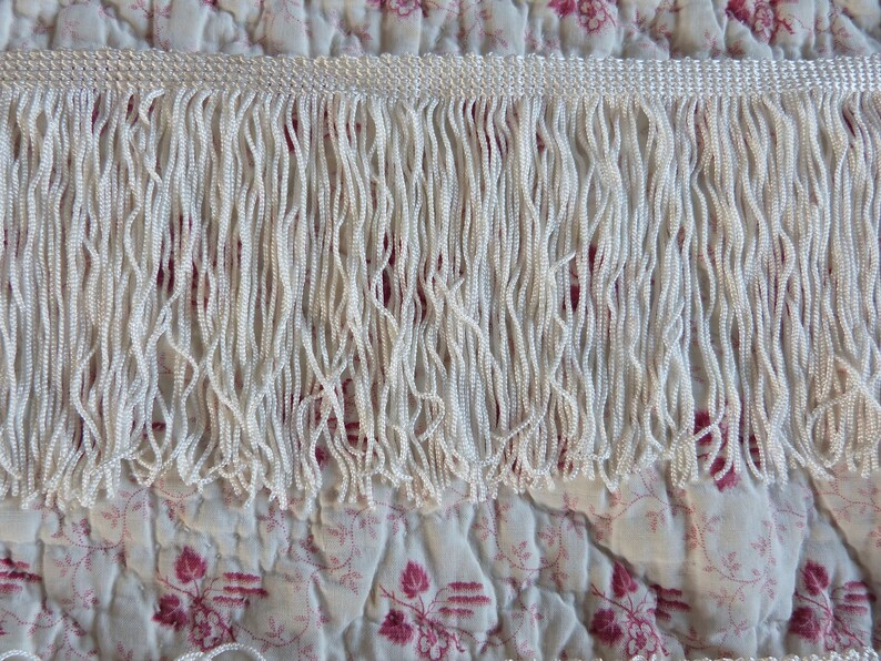 May include: White fringe trim with a subtle sheen. The fringe is made of small, tightly woven strands of fabric.