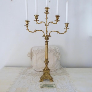 May include: A tall, gold-toned metal candelabra with five arms and a decorative base. The candelabra is designed to hold candles.