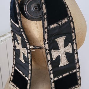 May include: Black velvet stole with a gold cross design and diamond-patterned trim. The stole has a fringe at the bottom and is displayed on a mannequin. A religious garment.