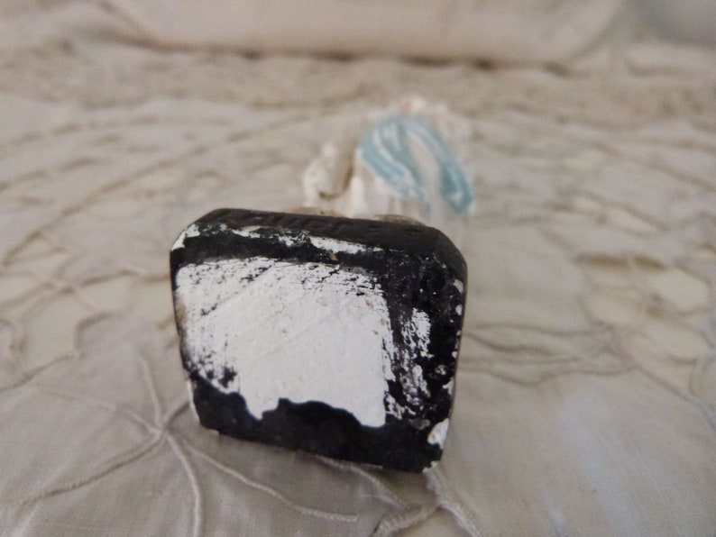May include: A white ceramic figurine of a woman wearing a blue dress. The figurine is standing on a black base with white paint.