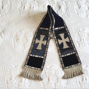 May include: A dark blue scarf with a gold cross design and fringe. The scarf has a velvet texture and is decorated with gold trim. The crosses are centered on the scarf.