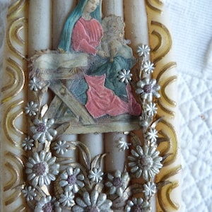 May include: A white candle with a religious image of Mary and baby Jesus in a manger. The image is surrounded by silver and gold floral accents.