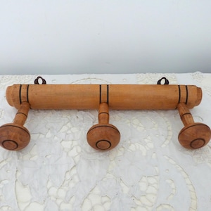 Puede incluir: Perchero de pared de madera con tres ganchos. El perchero está hecho de madera natural con detalles en marrón oscuro.