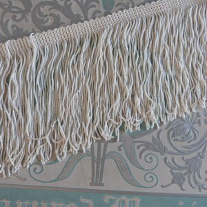 May include: White fringe trim with a beaded texture. The fringe is approximately 1 inch in length.