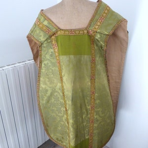 May include: A green and gold liturgical vestment with a floral pattern. The vestment is displayed on a mannequin. The trim is gold with red accents. The fabric has a sheen. The vestment is a religious garment.