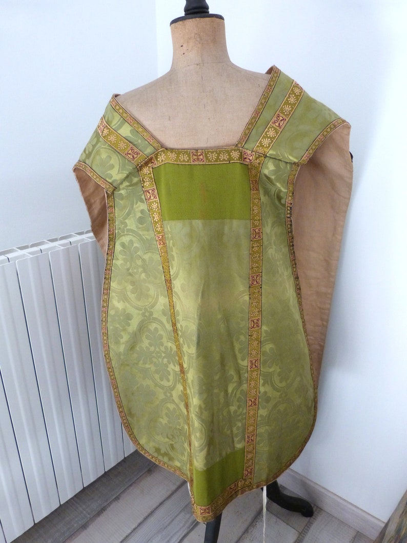 May include: A green and gold liturgical vestment with a floral pattern. The vestment is displayed on a mannequin. The trim is gold with red accents. The fabric has a sheen. The vestment is a religious garment.